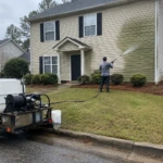 Worker pressure washing algae off vinyl siding on a two-story home in the Upstate SC