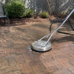 Surface cleaner on a brick paver patio with chairs pushed aside and a wood fence behind